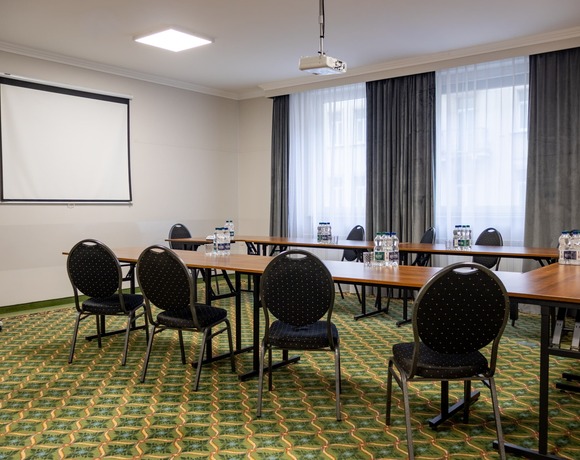 Šviesi konferencijų salė su U formos stalų išdėstymu, projektoriumi, ekranu ir konferencine lenta – visiškai įrengta verslo erdvė netoli metro stoties objekte, siūlančiame viešbutį Varšuvoje.