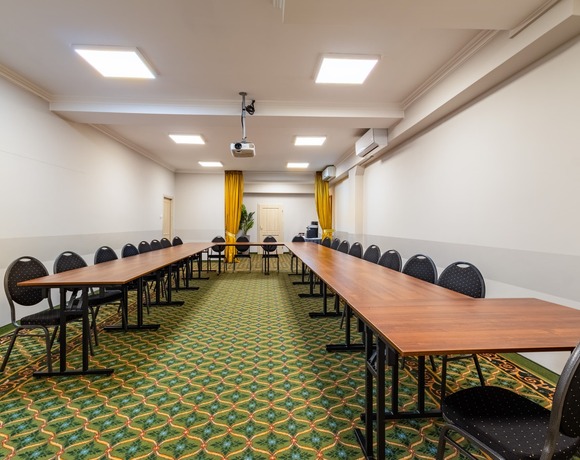 Conference room with tables in a horseshoe layout and a projector suspended from the ceiling, viewed from the open area inside the layout.