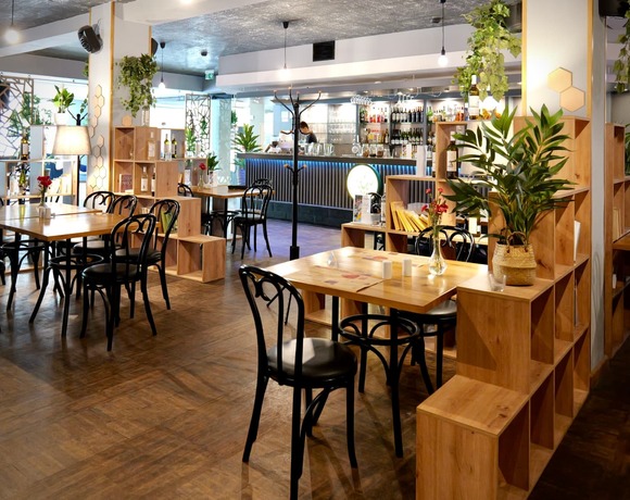Modernes Hotelbistro mit Holztischen, schwarzen Stühlen, beleuchtetem Tresen, Hängepflanzen und Barkeeper beim Mixen
