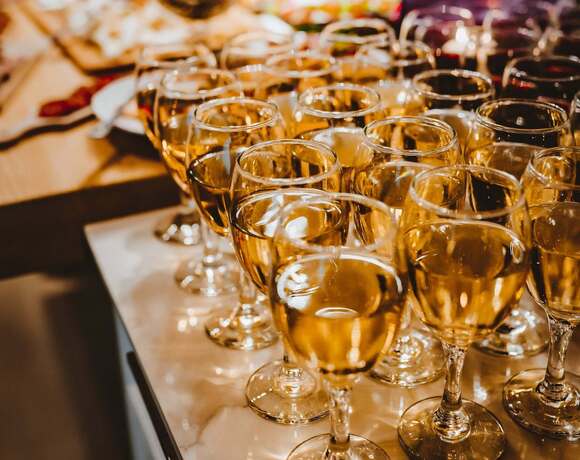 Reihen mit Weingläsern voller Weißwein auf Marmorbuffet, warme Beleuchtung für einen Empfang