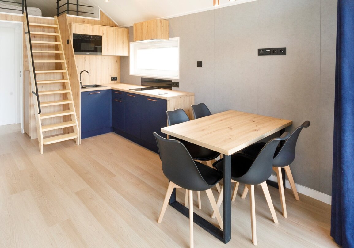 Kompaktowa kuchnia w apartamencie z drewnianymi szafkami, granatowymi frontami, drabiną na antresolę i jadalnią na cztery osoby.