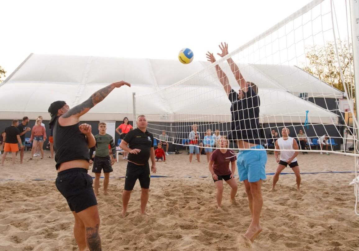 Goście grający w siatkówkę plażową na piaszczystym boisku hotelowym z widzami w tle