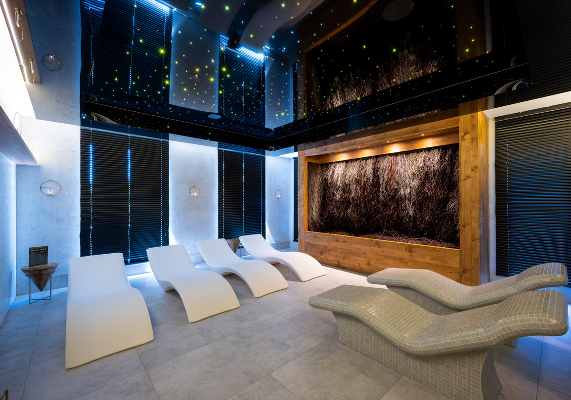 Nowoczesne miejsce relaksu z zakrzywionymi leżakami, ścianą z naturalnych gałęzi i delikatnym oświetleniem strefy spa
