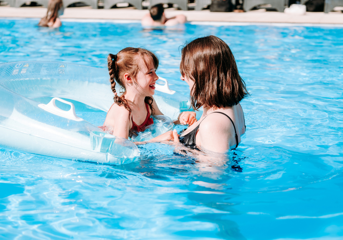 Dziecko na przezroczystym dmuchanym kole bawi się z kobietą w basenie hotelowym w słoneczny dzień