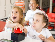 Děti si hrají v hotelovém dětském klubu a mačkají velké červené tlačítko na stole