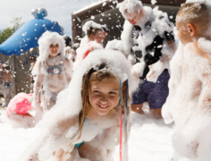 Děti si venku na slunném dni užívají zábavu ve velkém pěnovém parku u hotelu.