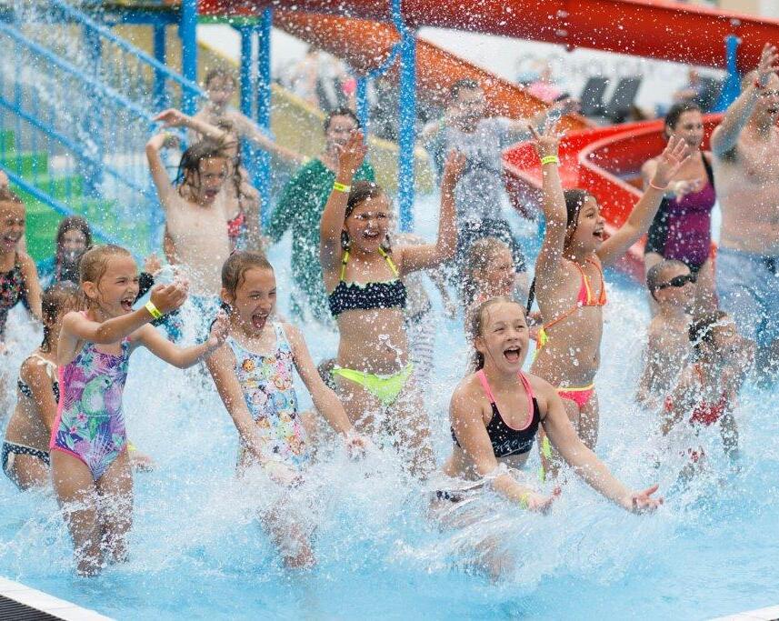 Kinder spielen und spritzen Wasser im Pool mit bunten Wasserrutschen im Hintergrund.