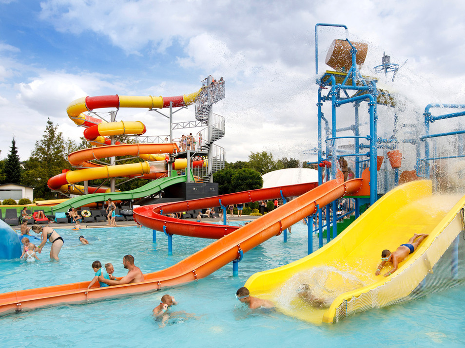 Pestrý vodní park s barevnými skluzavkami a bazénem, děti si hrají a plavou v slunečném rodinném prostředí.