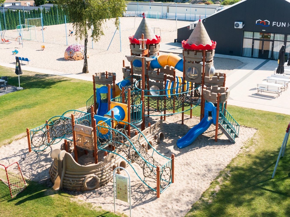 Plac zabaw w hotelu Fun House z zamkową strukturą, zjeżdżalniami i ściankami do wspinaczki na trawie i piasku.
