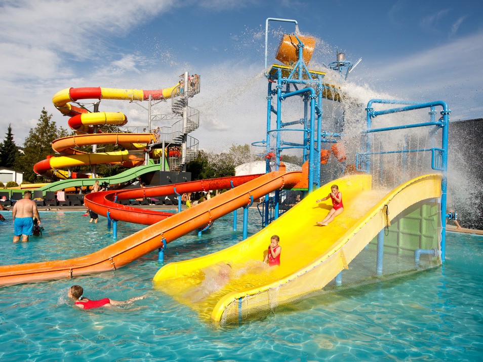 Vibrant water park with slides and water features, children and adults enjoying the outdoor pool on a sunny day.