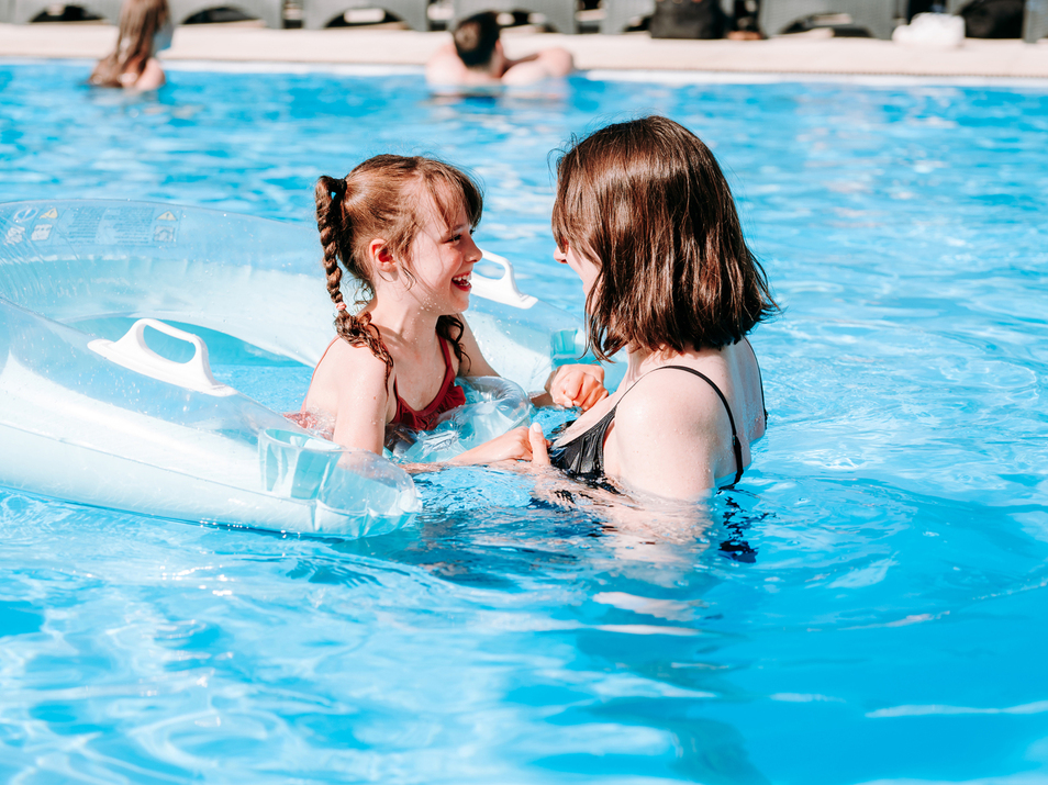 Child on transparent inflatable ring playing with woman in hotel pool on a sunny day