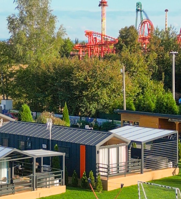 Nowoczesne domki letniskowe z tarasami na tle parku rozrywki z kolejką górską i wieżą widokową