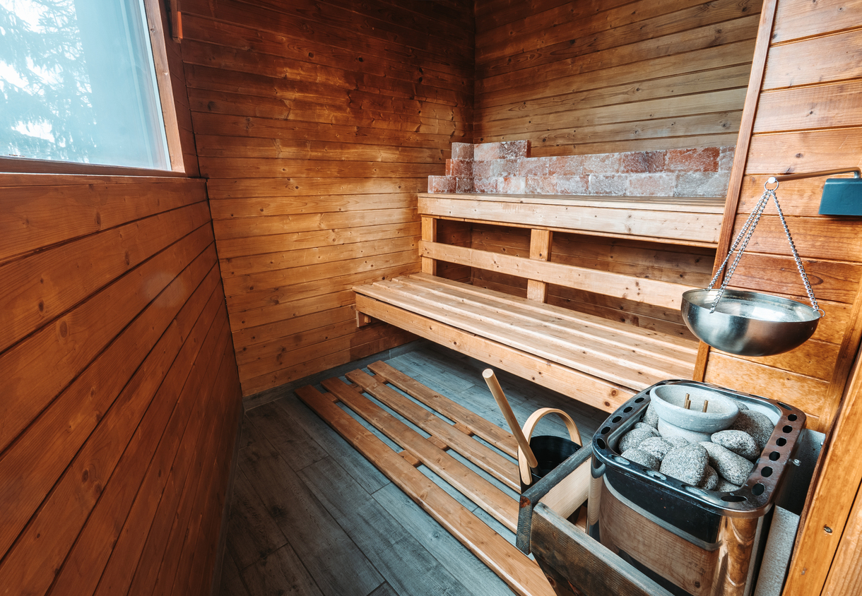 Drewniana sauna hotelowa z piętrowymi ławkami, piecem z kamieni, wiaderkiem i chochlą oraz ścianą z bloków solnych jako oparciem