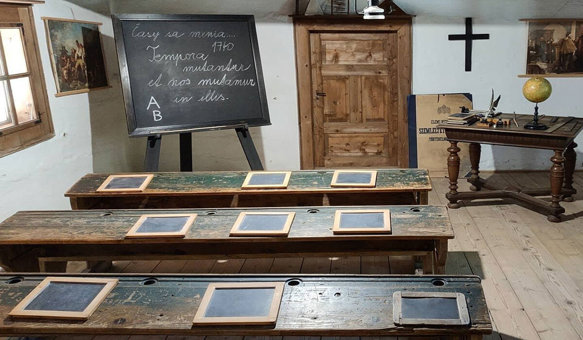 Historic 19th-century schoolroom exhibit with worn wooden benches, individual slates, chalkboard and teacher's desk with globe.