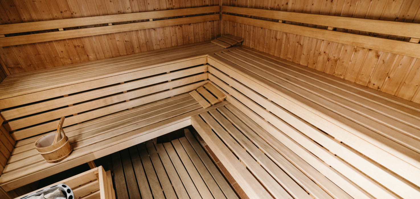 Wood-paneled hotel sauna with tiered wooden benches, bucket and ladle, and hot-stone heater for relaxing steam.