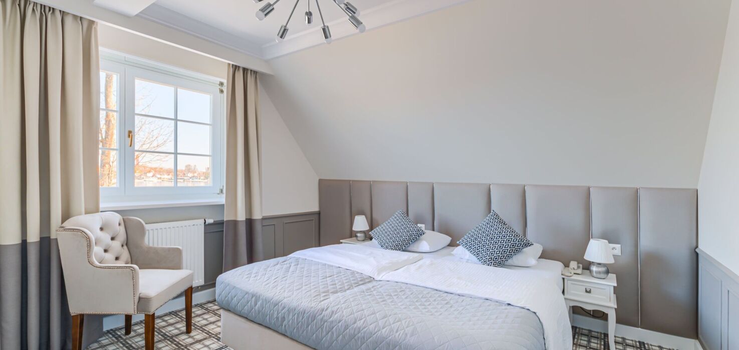 Sypialnia apartamentu z dużym łóżkiem, fotelem i oknem z widokiem