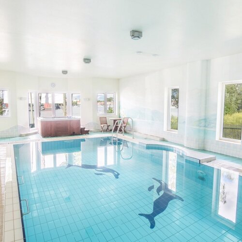 Kryty basen hotelowy z jasnoniebieskimi płytkami i oknami z widokiem na jezioro