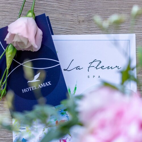Różowe kwiaty karta do pokoju Hotelu Amax oraz menu La Fleur Spa na drewnianym stole