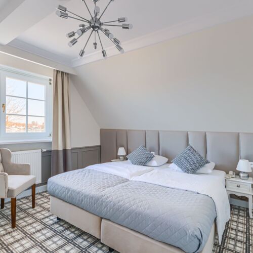 Sypialnia apartamentu z dużym łóżkiem, fotelem i oknem z widokiem