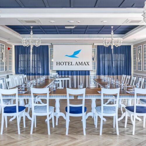 Sala konferencyjna Hotelu Amax ze stołami i krzesłami ustawionymi w podkowę z rzutnikiem na ścianie