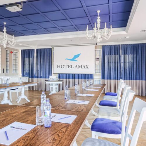 Sala konferencyjna Hotelu Amax ze stołami i krzesłami ustawionymi w podkowę z rzutnikiem na ścianie