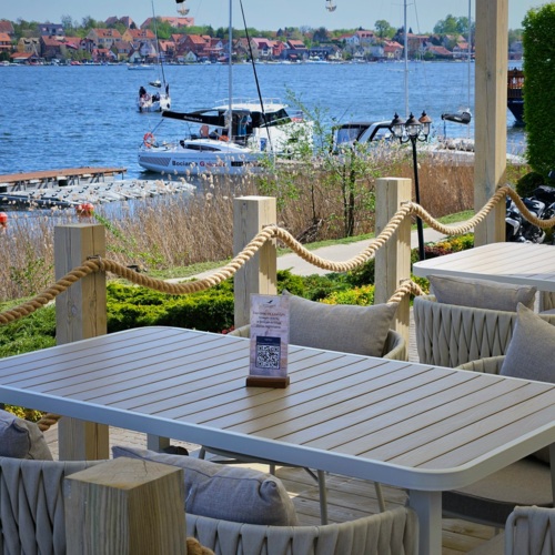 Widok na stolik restauracyjny na tarasie z widokiem na jezioro i promenadę Mikołajek