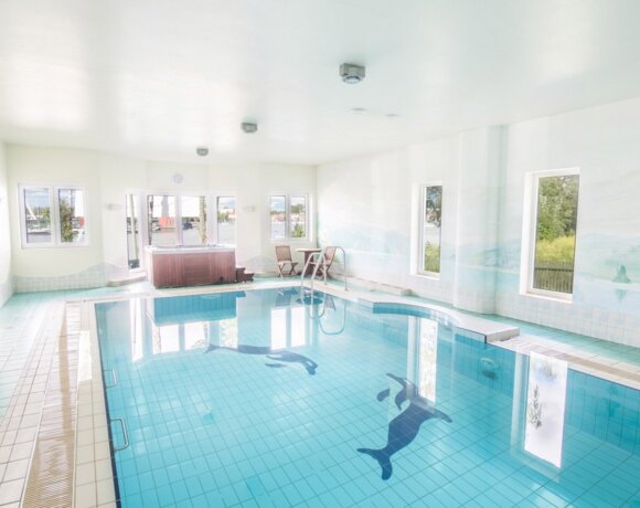 Kryty basen hotelowy z jasnoniebieskimi płytkami i oknami z widokiem na jezioro