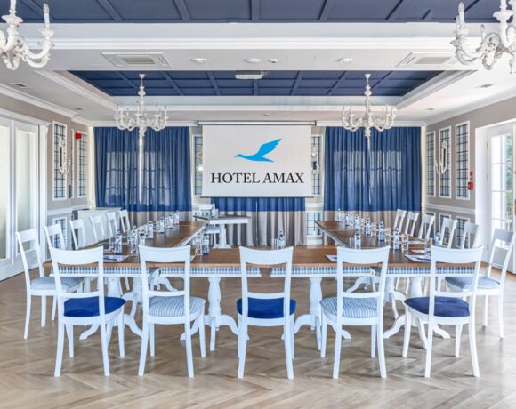 Sala konferencyjna Hotelu Amax ze stołami i krzesłami ustawionymi w podkowę z rzutnikiem na ścianie