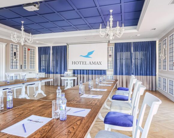 Sala konferencyjna Hotelu Amax ze stołami i krzesłami ustawionymi w podkowę z rzutnikiem na ścianie