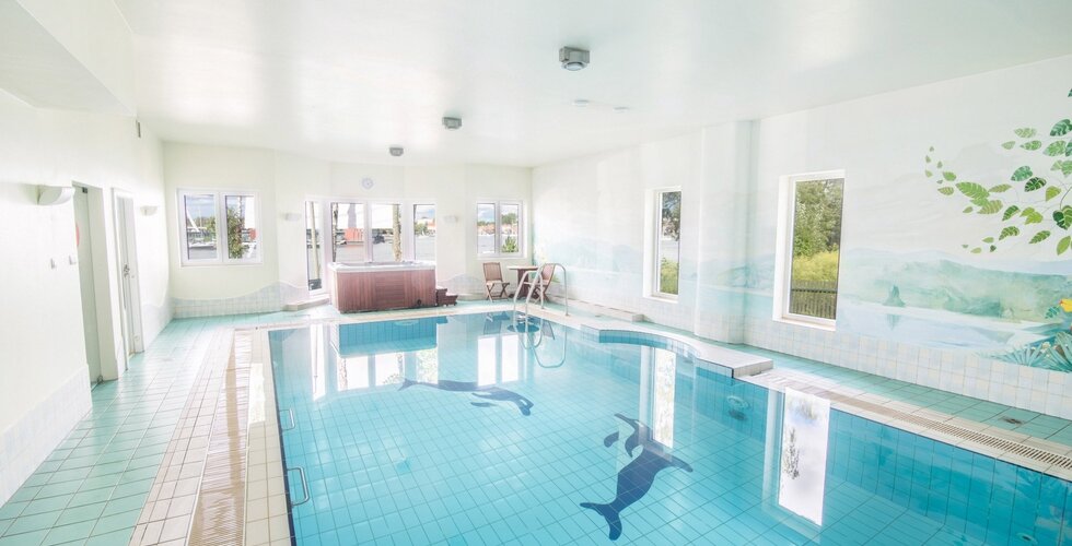 Kryty basen hotelowy z jasnoniebieskimi płytkami i oknami z widokiem na jezioro