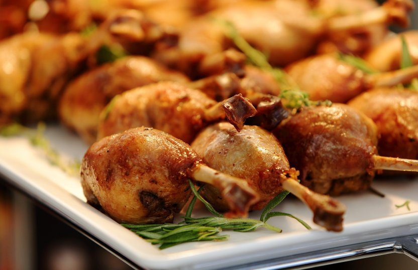 Goldbraun gebratene Geflügel‑Lollipops auf weißer Platte, mit Rosmarin garniert, elegante Hotelvorspeise