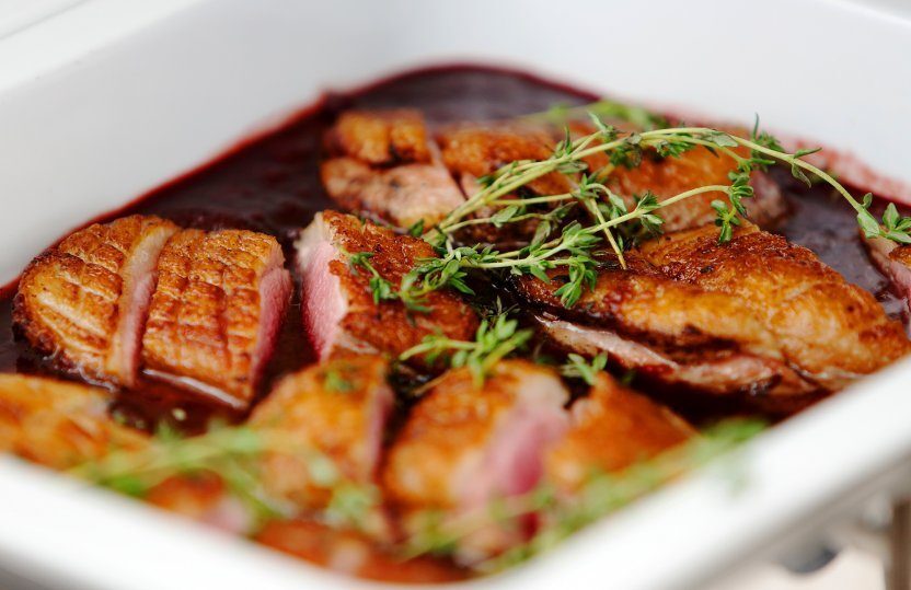 Gebratene Entenbrustscheiben in Rotweinjus, garniert mit frischem Thymian, serviert in einer weißen Schale