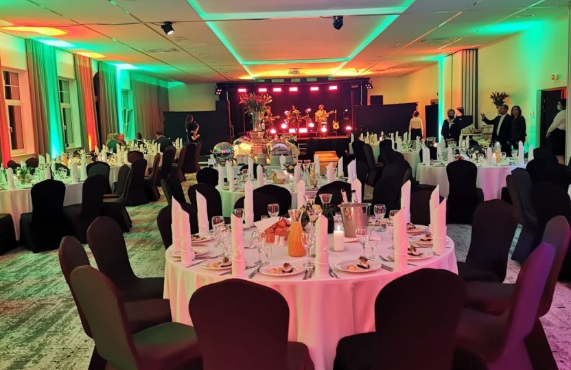 Eleganter Bankettsaal im Hotel für Abendessen, runde Tische mit weißen Tischdecken, Bühne mit Liveband und stimmungsvolle Beleuchtung