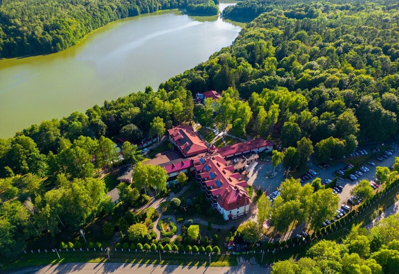 Seeresort mit roten Dächern, gepflegten Gärten, Parkplätzen und Waldwegen am ruhigen See, umgeben von dichtem Grün