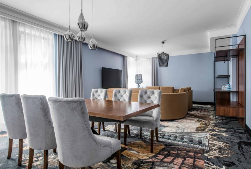 Geräumige Suite mit Wohn- und Essbereich, Holztisch mit sechs gepolsterten Stühlen, geschwungenes Sofa, Flachbild-TV und bodentiefe Vorhänge