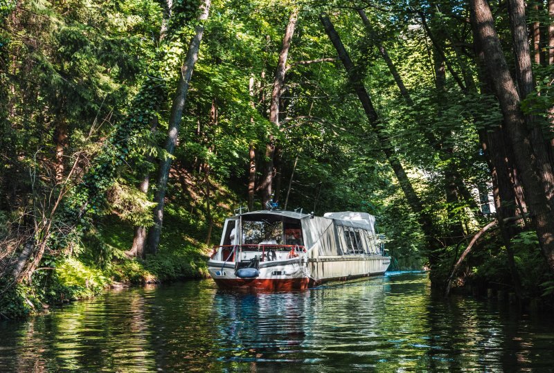 Überdachtes Ausflugsboot fährt durch einen schattigen Waldkanal unter dichtem Blätterdach und bietet eine ruhige Flussfahrt.