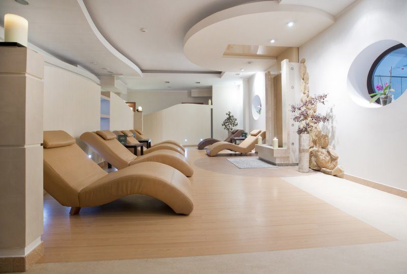 Spa-Entspannungsbereich mit geschwungenen beigen Liegen, sanfter Beleuchtung, Kerzen und Bullaugenfenster