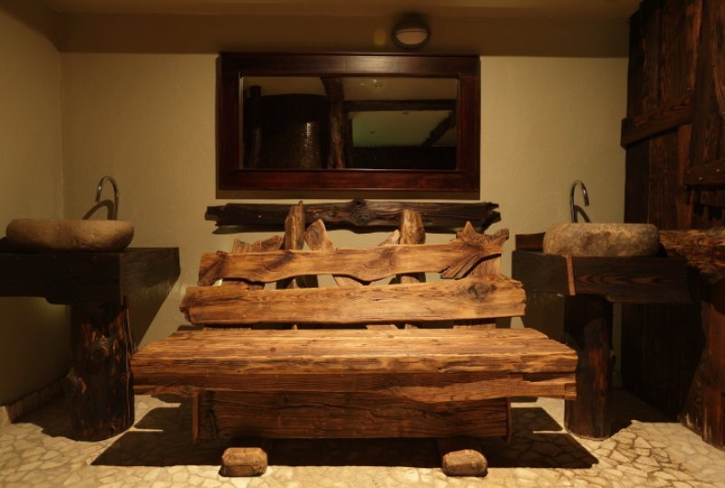 Rustikale, geschnitzte Holzbank mit Konsole und Steinwaschbecken, warmes Spa‑Ambiente