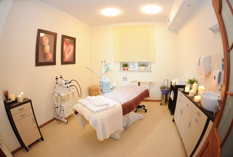 Gemütlicher Behandlungsraum mit Massageliege, frischen Handtüchern, Kerzenlicht, professionellen Kosmetikgeräten und Waschbecken.