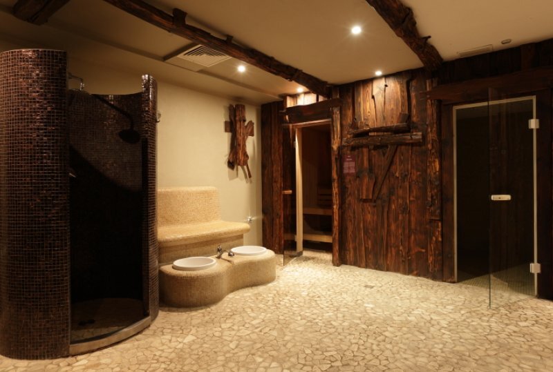 Warmer, holzverkleideter Spa-Bereich mit privater Sauna, Mosaikdusche, kieseligem Boden, geschwungener Ruhebank und zwei Fußbecken.