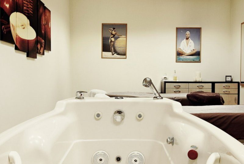 Whirlpoolwanne und Massageliege in ruhigem Spa-Behandlungsraum mit neutraler Einrichtung, Kerzen und gerahmter Kunst