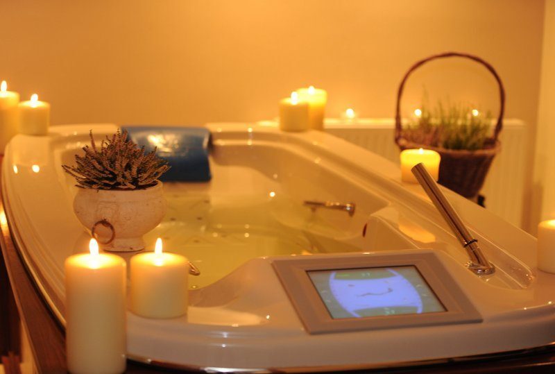 Whirlpool-Badewanne mit blauem Nackenkissen, Touchscreen-Steuerung, brennenden Kerzen und Pflanzen, warme Spa-Atmosphäre