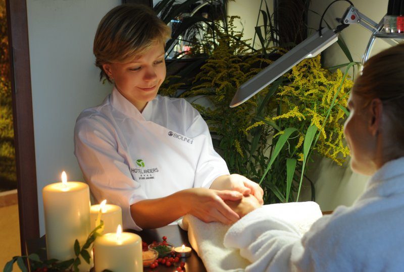 Therapeutin gibt entspannende Handmassage auf Handtuch-bedeckter Liege, Kerzen und Pflanzen schaffen ruhige Spa-Atmosphäre