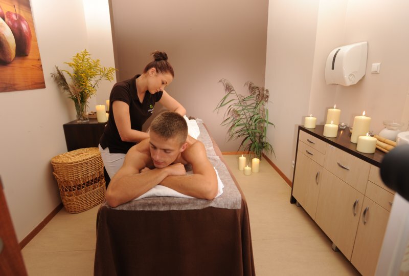 Mann erhält entspannende Rückenmassage im Hotel-Spa, umgeben von Kerzen, Pflanzen und warmem Licht