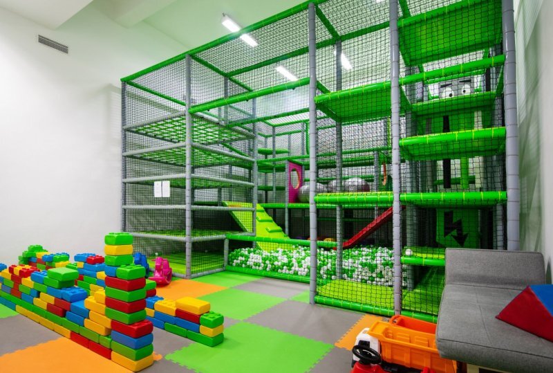 Innen-Kinderspielbereich mit mehrstöckigem Softplay, Bällebad, Rutschen, bunten Schaumstoffbausteinen und Sitzbank.