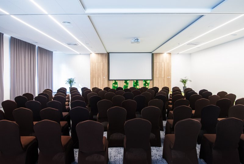 Moderner Konferenzraum im Hotel mit Reihen bezogener Stühle, Leinwand, Holzakzenten und Topfpflanzen