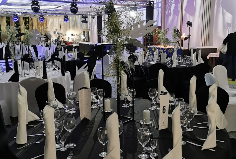 Elegantes schwarz-weißes Bankett mit runden Tischen, Blumenarrangements, gefalteten Servietten, Kerzen, Glasgedeck und Bühne.