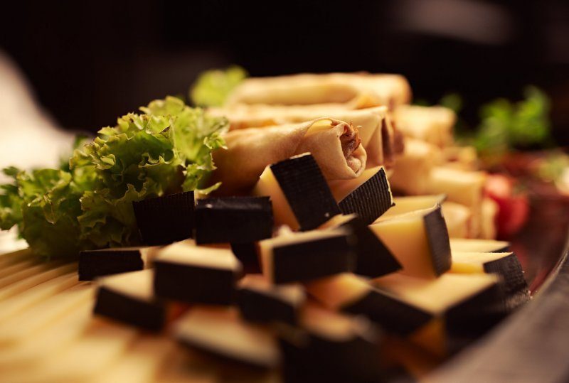 Vorspeisenplatte: gestapelte Frühlingsrollen, Käsewürfel mit dunklem Rand und Salatgarnitur