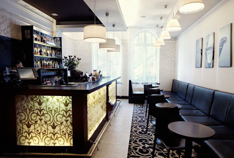 Elegante Hotelbar mit beleuchtetem, ornamentiertem Tresen, Spirituosenregalen, Hängeleuchten und Ledersitzbank.