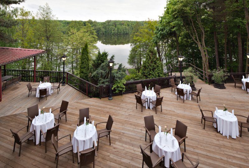Holzterrasse am See mit weiß gedeckten Tischen, Laternenbeleuchtung und ruhigem Blick auf Wald und Wasser